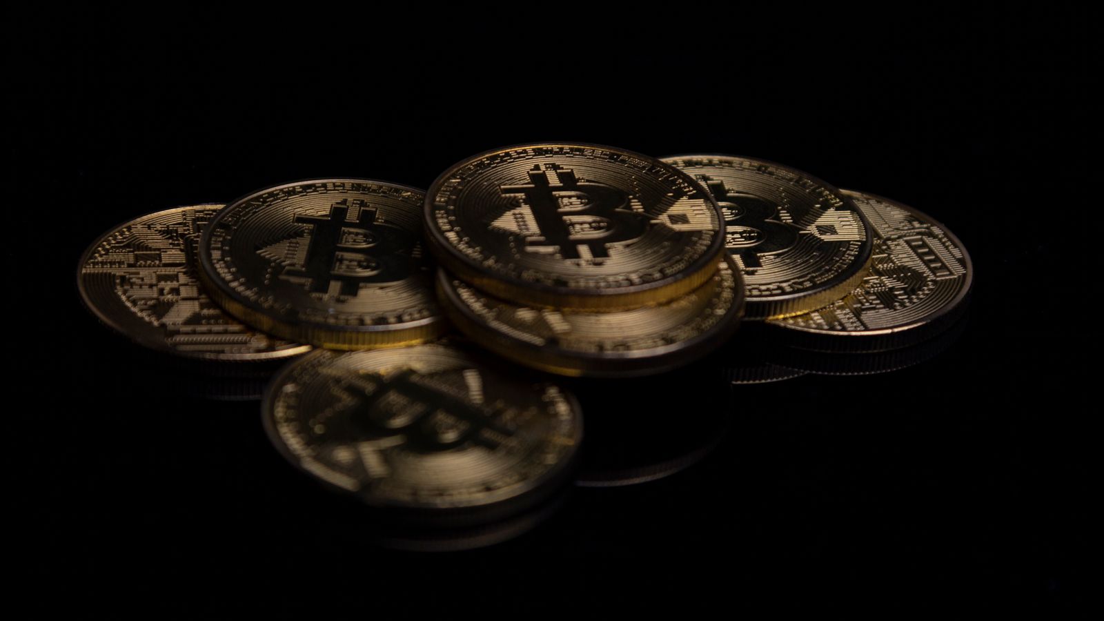 Yansıtıcı siyah zemin üzerinde dizilmiş altın Bitcoin paralarının yakın çekimi — Bitcoin 86.000 doları gördü, ETF yatırımcısı kâra geçti ve Türkiye'de 1 Bitcoin 4,18 milyon lira oldu